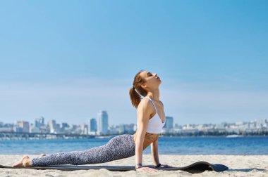 Genç ince atletik kadın yoga egzersizleri yapar ve şehir arka plan ile kum plajda uzanan. Sağlıklı yaşam tarzı, sabah egzersizleri, meditasyon.