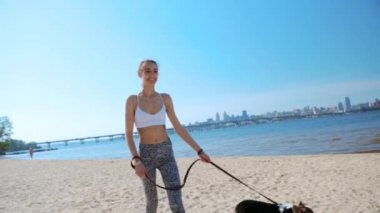 beautiful young slim athletic woman walking with cute tricolor Welsh Corgi dog on the sand beach at sunny morning.