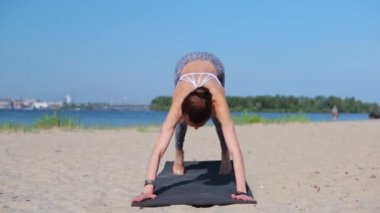 Genç fitness hanımı Asya kökenli beyaz ırk yoga esneme egzersizleri yapıyor. Kumsalda yoga-asanas yapan bir kadın. Genç zayıf atletik kadın Surya yapıyor