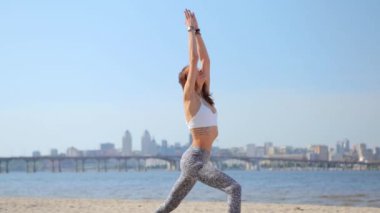 Kumsalda yoga-asanas yapan bir kadın. Yoga yapan zayıf, atletik bir kadın. Asana 'da duruyor. Elleri havada, mavi gökyüzü geçmişi var..