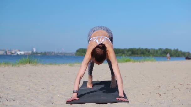 Young fitness lady mixed race of Asian Caucasian ethnicity make yoga stretching exercises. Woman practicing performing yoga-asanas uotdoors on the sand beach. young slim athletic woman making surya — ストック動画