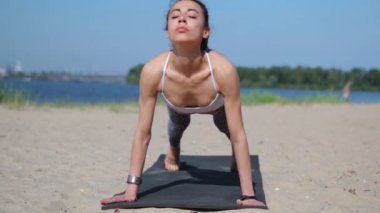 Genç fitness hanımı Asya kökenli beyaz ırk yoga esneme egzersizleri yapıyor. Kumsalda yoga-asanas yapan bir kadın. Genç zayıf atletik kadın Surya yapıyor