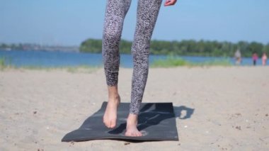 Genç fitness hanımı Asya kökenli beyaz ırk yoga esneme egzersizleri yapıyor. Kumsalda yoga-asanas yapan bir kadın. Genç zayıf atletik kadın Surya yapıyor
