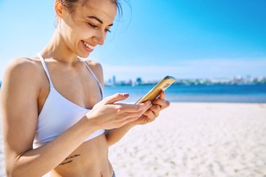 Deniz arka plan ile kum şehir plajda güzel seksi mutlu kadın Closeup portre, telefon bakarak ve gülümseyerek. Yaz konsepti.