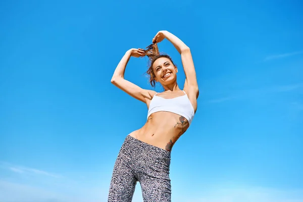 Szczęśliwy uśmiechnięta kobieta sportowa z opalony dopasowanie ciała i tatuaż stwarzające przeciwko błękitne niebo. — Zdjęcie stockowe