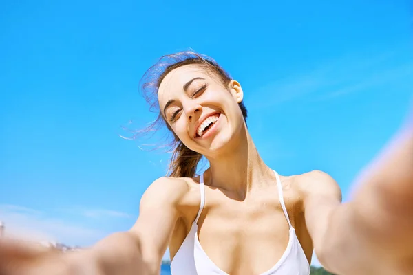 Portrait of beautiful happy woman taking a selfie on the camera phone with blue sky on background. Summertime and leisure concept. — Stock Photo, Image