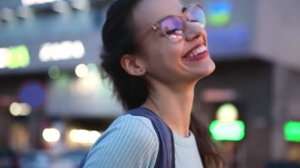 Portrait urbain en plein air d'une jeune femme belle adulte en lunettes, posant en plein air dans la rue sur fond de lumières de la ville de nuit. jeune femme moderne marchant ville à la soirée d'été — Video