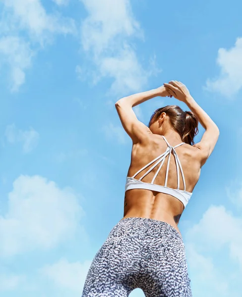 Houkutteleva urheilu nainen ruskettunut istuvuus kehon poseeraa vastaan sininen taivas pilvet. selkä wiew . — kuvapankkivalokuva