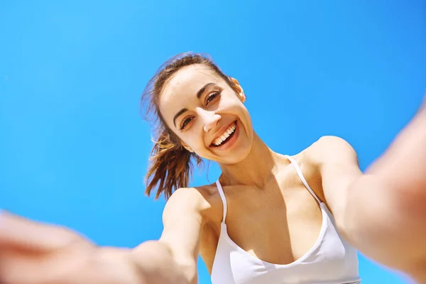 Portrett av en vakker, lykkelig kvinne som tar en selfie på kameratelefonen med blå himmel i bakgrunnen. Sommer- og fritidsbegrep . – stockfoto