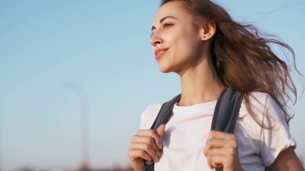 Beyaz t-shirt ve kırmızı etek rahat genç güzel kadın mavi gökyüzü arka plan üzerinde duruyor ve gün batımıbakıyor. — Stok video