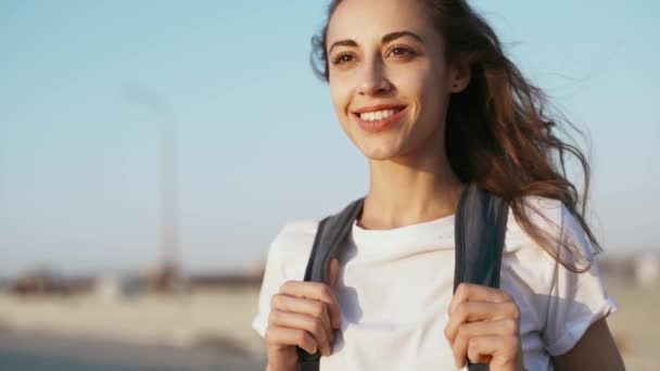 白いTシャツと赤いスカートを着たリラックスした若いかわいい女性は、青い空の背景に立って、夕日を見ています. — ストック動画