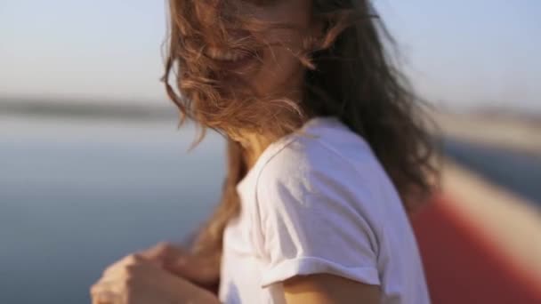Giovane donna felice guardando tramonto serale sul mare. bella ragazza è in piedi sul ponte, godendo la vista del tramonto e la luce del vento fresco — Video Stock