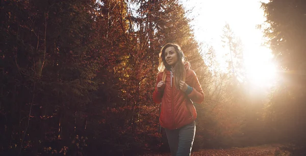Mujer excursionista con mochila con chaqueta roja está caminando a través de un bosque de otoño de niebla por la mañana y disfrutar de la salida del sol . — Foto de Stock