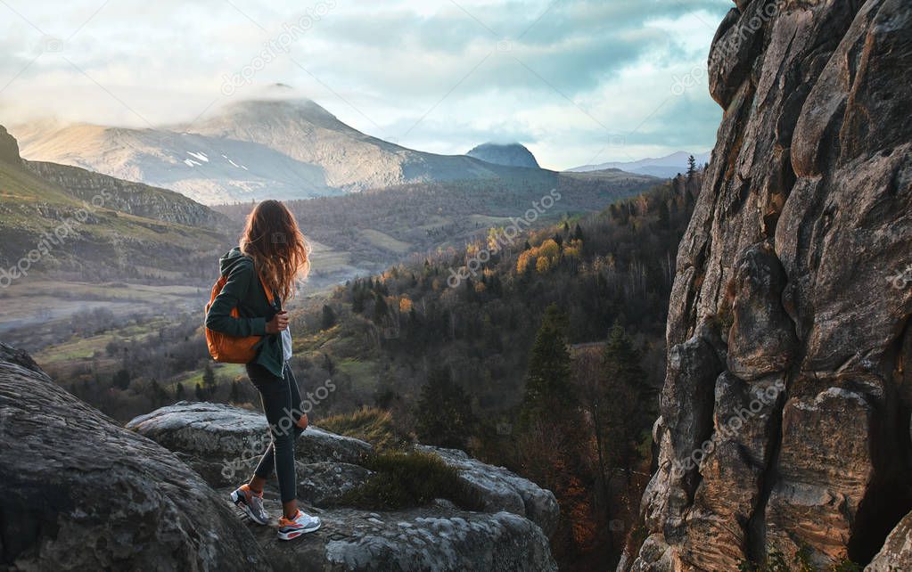 woman standing on edge of cliff against background of sunrise