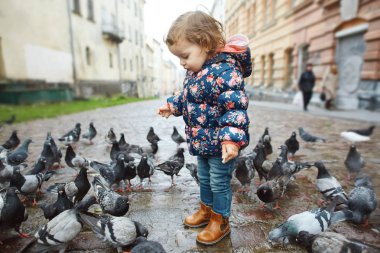 Komik bebek kız sonbahar günü sokakta güvercinler arasında duran.