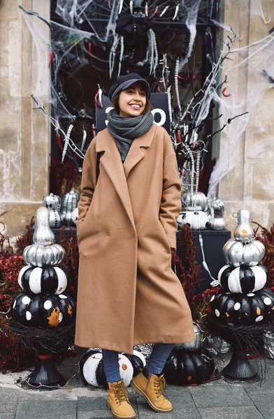 Осенний образ жизни портрет красивой улыбающейся женщины в бежевом пальто, теплый шарф и шляпа на улице с Хэллоуином фоне . — стоковое фото