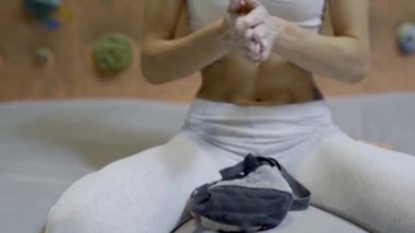 Kadın tırmanışçı, kapalı spor salonuna tırmanmadan önce beyaz tebeşir tozuyla elleri tebeşirliyor. Kadın tırmanmaya hazırlanıyor..