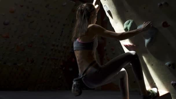 Mujer joven Escalador de rocas está escalando en el interior escalada gimnasio. slim bonita mujer ejercicio en interior escalada gimnasio pared — Vídeos de Stock