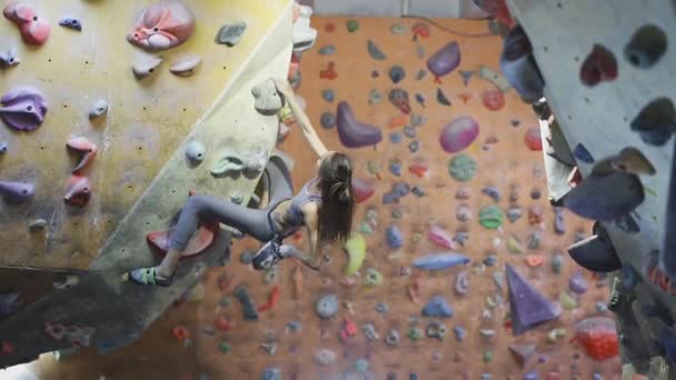 Ung kvinna rock klättrare klättrar en bouldering på inomhus klättring gym. smal Fitness vacker kvinna att göra några hårda drag och rädd för att göra sista långa flytta, misslyckade försök, nederlag, långsam — Stockvideo