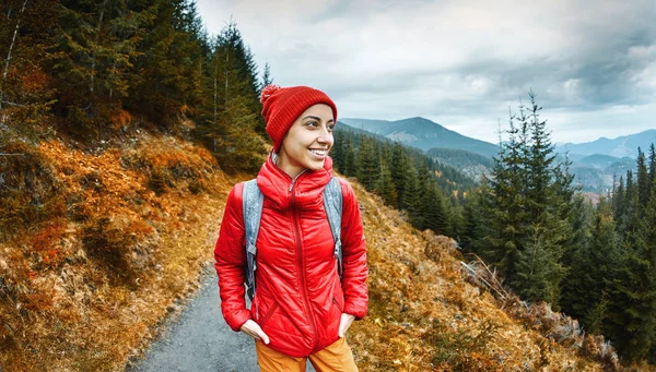 Randonneur femme avec sac à dos, veste rouge et pantalon orange, debout sur le fond des montagnes — Photo