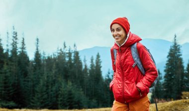 kırmızı ceket ve turuncu pantolon giyen küçük sırt çantası ile kadın yürüyüşçü Karpatlar dağlarda çam ormanları ile iz yürür