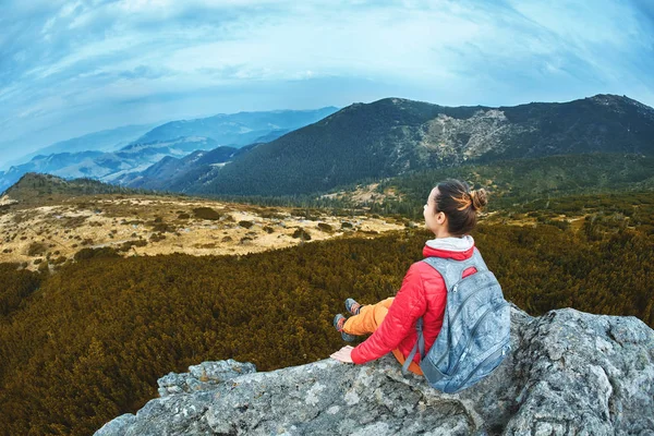 Mujer excursionista en chaqueta roja sentado en el acantilado en el punto de vista alto en las montañas de los Cárpatos — Foto de Stock