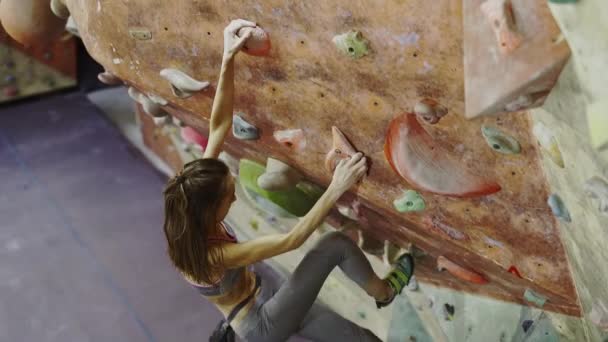 Mujer joven Escalador de rocas está escalando una roca en el gimnasio de escalada interior. slim bonita mujer haciendo algunos movimientos difíciles y conseguir la cumbre . — Vídeos de Stock