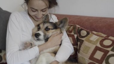Evde kanepede yatan onu sevimli Galce Corgi köpek ile mutlu gülümseyen kadın Portresi. Komik köpek yavrusu kucaklayan güzel esmer kadın