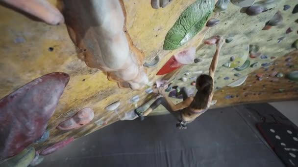 Horolezec z mladé ženy šplhá na boulderingu v interiérech v tělocvičně. štíhlá pěkná ženská dělá nějaké tvrdé pohyby a dostala vrchol. — Stock video