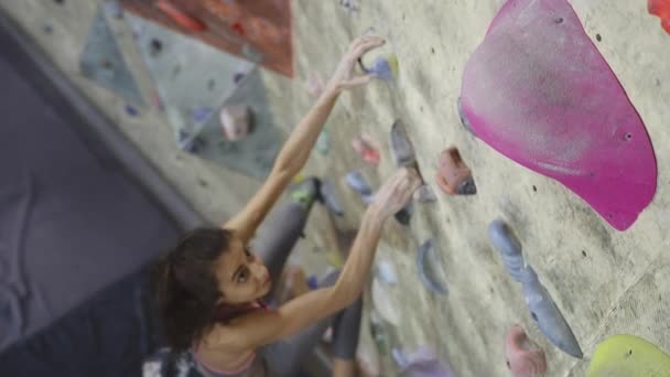 Genç Kadın Kaya dağcı Kapalı tırmanma Spor Salonu'nda bir bouldering tırmanıyor. ince güzel Kadın bazı sert hamle yapma ve zirve almak. — Stok video