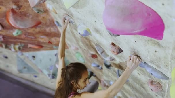 Mujer joven Escalador de rocas está escalando una roca en el gimnasio de escalada interior. slim bonita mujer haciendo algunos movimientos difíciles y conseguir la cumbre . — Vídeos de Stock