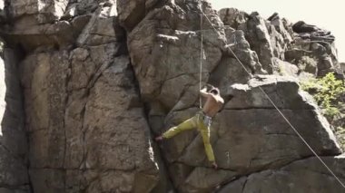 atletik adam kaya tırmanıcı bir uçuruma tırmanıyor, ulaşan ve sürükleyici tutun.