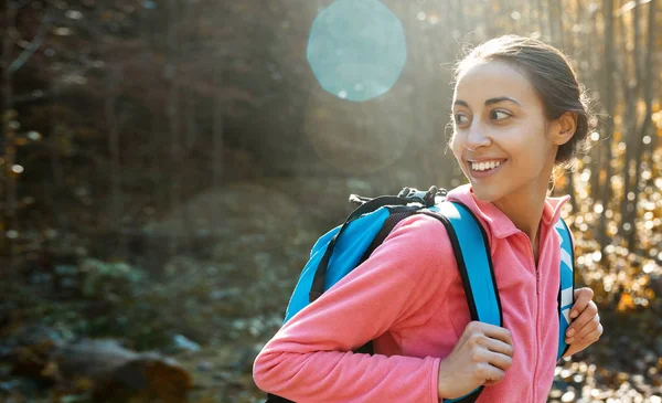 Retrato de mujer excursionista con mochila pequeña, con chaqueta de lana rosa, de pie sobre el fondo de bosques de pino en las montañas leñosas Cárpatos, oeste de Ucrania. feliz mujer sonriente mirando hacia atrás — Foto de Stock