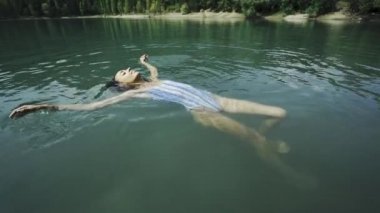 Güzel, ince, seksi, mavi mayo giymiş mutlu kadın güneşli yaz gününde dağ gölünde dinleniyor, yüzüyor ve tatlı suyun tadını çıkarıyor..