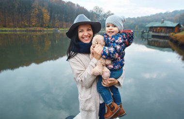 Göl kenarında sonbahar parkında yürürken kızı ile mutlu anne.