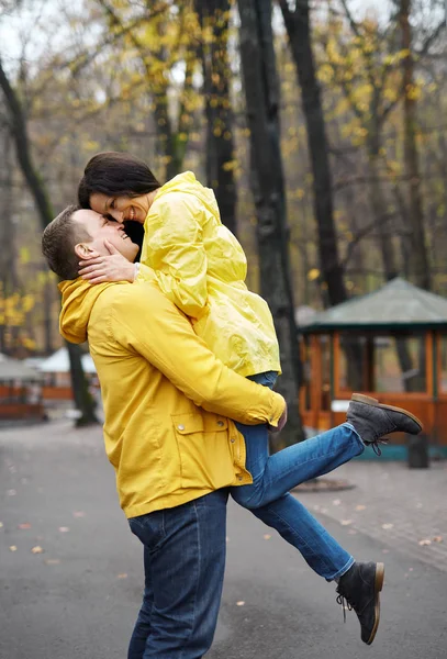 一对穿着黄色夹克的夫妇拥抱和亲吻，走在秋天的公园。快乐的年轻家庭共度时光. — 图库照片