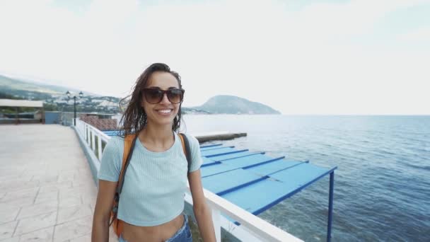 Retrato exterior de hermosa mujer deportiva sexy con estilo en traje de baño negro y gorra blanca caminando a lo largo de la bahía en la playa, contra un mar azul en el día soleado . — Vídeo de stock