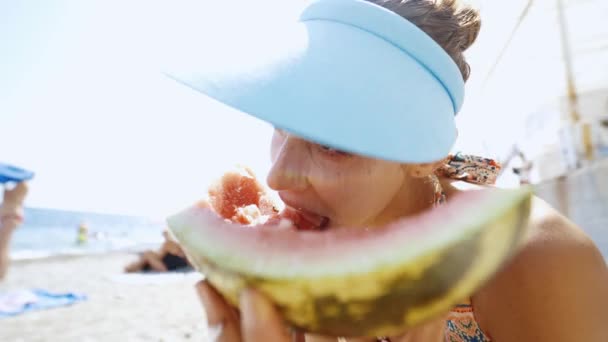 Szerokokątny strzał śmieszne młoda dziewczyna na plaży jedzenia duży kawałek arbuza — Wideo stockowe