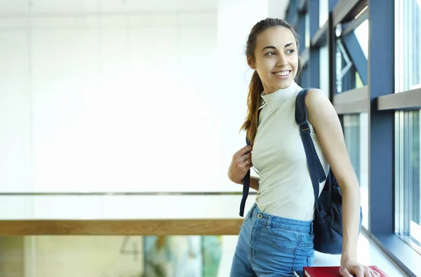 Bella giovane donna felice con uno zaino e quaderni all'interno di un campus universitario. Giovane studentessa universitaria con libri nel campus . — Foto Stock