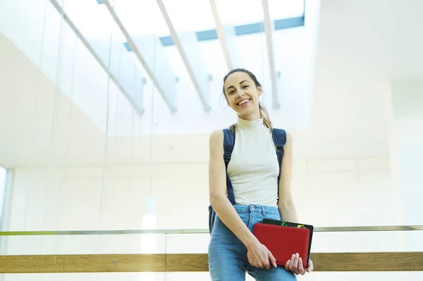 Belle jeune femme heureuse avec un sac à dos et des cahiers à l'intérieur d'un campus universitaire. Jeune étudiante universitaire avec des livres sur le campus . — Photo