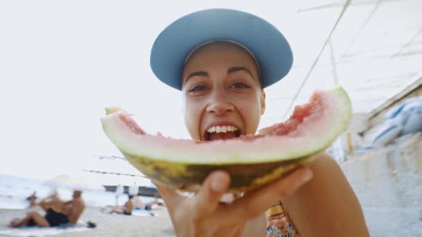 Amplio ángulo de tiro de divertida joven en la playa comiendo un gran pedazo de sandía — Vídeo de stock