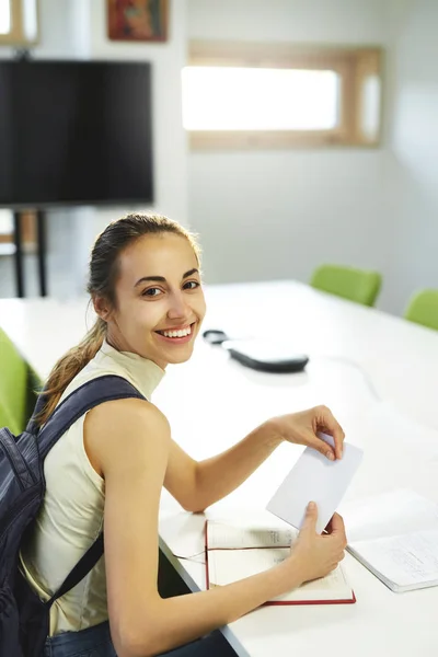 Ritratto di giovane studentessa sorridente di informatica seduta a tavola in aula, appunti di lettura e informazioni per il copybook — Foto Stock
