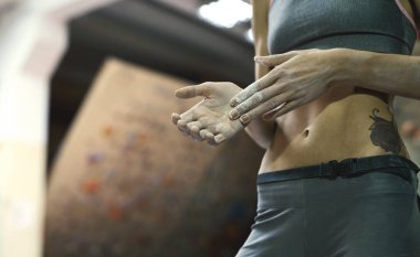 Kadın tırmanışçı, kapalı spor salonuna tırmanmadan önce beyaz tebeşir tozuyla elleri tebeşirliyor. Kadın tırmanmaya hazırlanıyor..