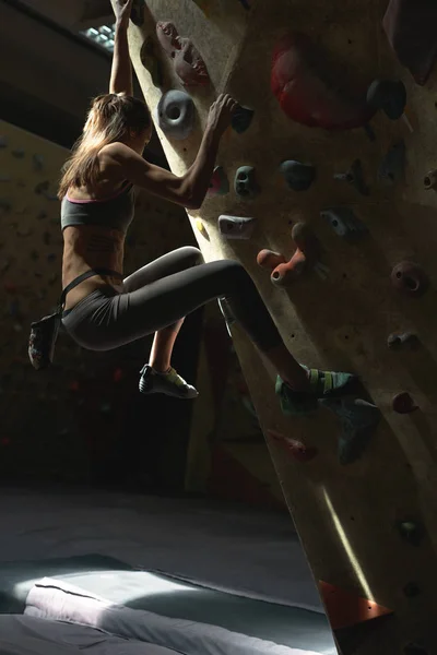 Mujer joven Escalador de rocas está escalando en el interior escalada gimnasio. slim bonita mujer ejercicio en interior escalada gimnasio pared —  Fotos de Stock