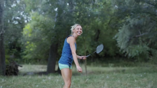 Jolie femme de fitness sportive souriante jouant au badminton dans le parc . — Video