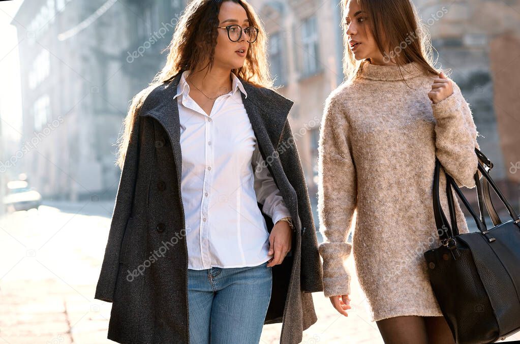 two beautiful fashionable stylish women walking city street at sunny warm autumn day