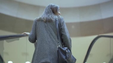 Arkaya bakan genç kadın yürüyen merdivene çıkıyor.