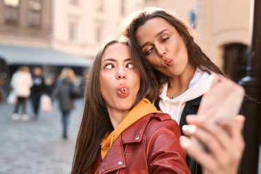Şehirdeki telefon kulübesinde fotoğraf çektirmek için komik suratlar yapan hoş genç kadınların portresi..