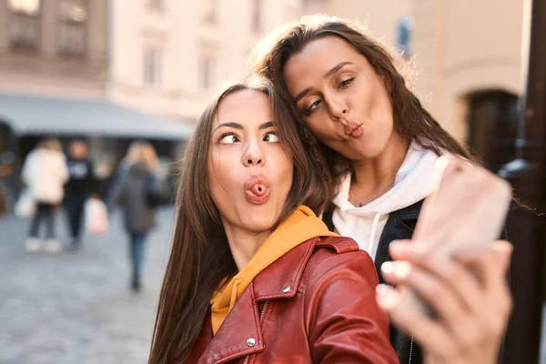 Portret uroczych młodych kobiet robi śmieszne twarze do zdjęcia na telefon uotdoors w mieście. — Zdjęcie stockowe