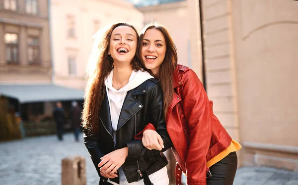 Lieflijke blanke vrouwen in gekleurde lederen motorjassen en hoodies poseren met een glimlach op straat op autmn dag. — Stockfoto